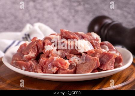 Fleisch mit Lammwürfelchen. Gehacktes rotes Fleisch auf einem Teller auf einem Steinboden. Metzgerprodukte. Nahaufnahme Stockfoto