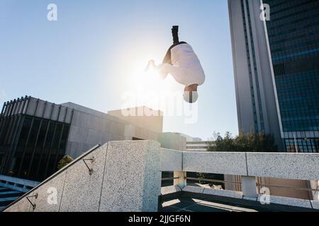 Ein sportlicher Mann übt Parkour und freies Laufen, indem er einen Frontflip von einem Hindernis im Freien aus macht. Sportlicher junger Mann, der extreme sportliche Aktivitäten übt o Stockfoto