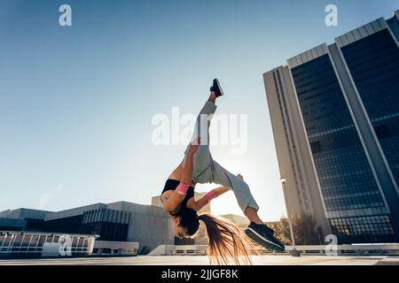 Eine urbane Frau, die in der Stadt einen Flashkick im Freien aufführt. Fit junge Sportlerin macht Frontflip. Stockfoto