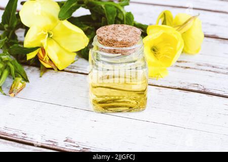 Ätherisches Öl der Nachtkerze in Glasflasche, gelbe Blumen auf weißem Tisch, alternative Medizin Stockfoto