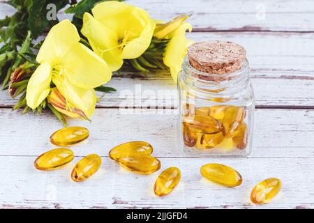 Nachtkerzenöl-Gel-Kapseln in Glasflasche, Pillen und gelbe Blumen auf Holztisch Stockfoto