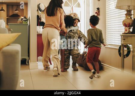 Freudige militärische Heimkehr. Glücklicher Soldat, der sich nach seinem Militärdienst mit seiner Frau und seinen Kindern wiedervereinigt. Fröhlicher Militärangehöriger umarmt seine Familie achtern Stockfoto