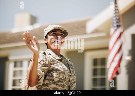 Fröhliche Soldatinnen, die lächelnd und stolz mit der Hand winkend vor ihrem Haus standen. Patriotische amerikanische Militärangehörige, die nach wie vor nach Hause kommt Stockfoto