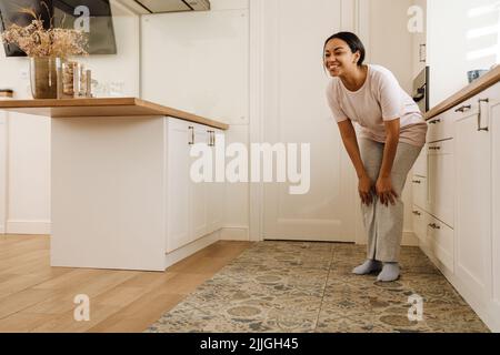 Junge hispanische Frau lächelt, während sie zu Hause in der Küche steht Stockfoto
