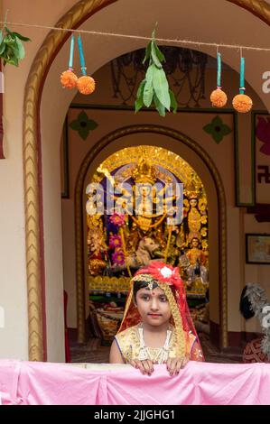 Howrah, Indien -26.. Oktober 2020 : Bengalisches Mädchen in festlichem Kleid, lächelnd und posiert mit Göttin Durga im Hintergrund, innen dekoriert Pandal. Stockfoto