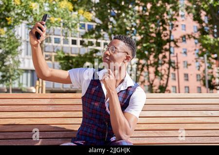 Junger afroamerikanischer Mann, der sein Smartphone benutzt, um ein Selfie zu machen oder einen Videoanruf zu tätigen Stockfoto