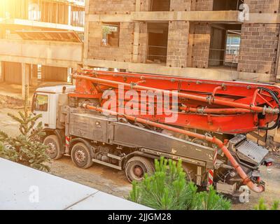 LKW mit einem leuchtend roten gefalteten Kran auf einer Baustelle vor einem unfertigen Haus Stockfoto