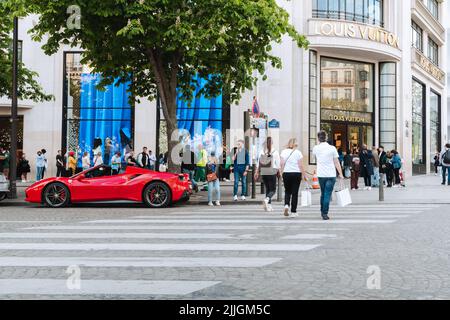 Luxusgeschäft von Louis Vuitton mit rotem Ferrari vorne und Tourist an der Champs-Élysées Straße in Paris. Stockfoto