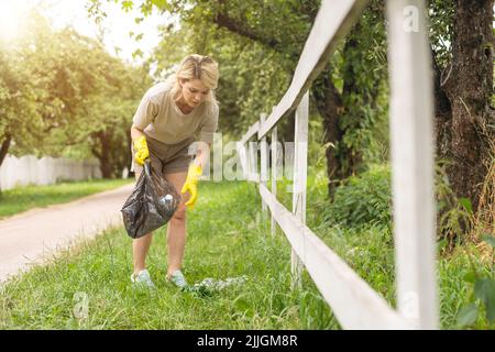 Frau trägt Latexhandschuhe, die Müll in den Müllbeutel nimmt, die gebrauchte Plastikflasche in der Hand hält, kümmert sich um den Planeten Stockfoto