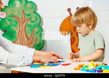 Junge mit Erwachsenen im Kindergarten legte Figuren auf den Tisch Stockfoto