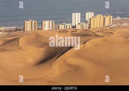 Die riesigen Sanddünen von Cerro Dragon mit der Stadt Iquique, Chile hinter der Küste des Pazifischen Ozeans. Stockfoto