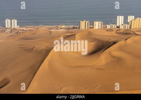 Die riesigen Sanddünen von Cerro Dragon mit der Stadt Iquique, Chile hinter der Küste des Pazifischen Ozeans. Stockfoto