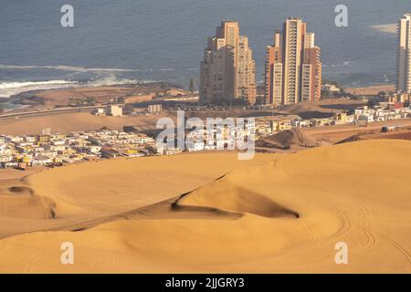 Die riesigen Sanddünen von Cerro Dragon mit der Stadt Iquique, Chile hinter der Küste des Pazifischen Ozeans. Stockfoto