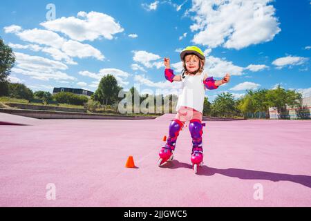 Kleines Mädchen in Helm und Schutz lernen, auf Rollen zu skaten Stockfoto