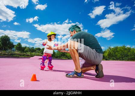 Vater lehren Mädchen auf Rollen zu stehen helfen ihr mit Händen Stockfoto