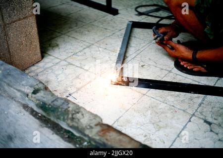 Asiatischer traditioneller Industriearbeiter, der die Eisenstücke bei der Arbeit schweißen kann Stockfoto