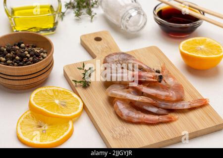 Rohe Garnelen auf Schneidebrett. Zitronenscheiben, Piment in Schüssel, Sojasauce auf dem Tisch. Draufsicht. Weißer Hintergrund Stockfoto