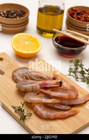 Rohe Garnelen auf Schneidebrett. Sojasauce in Glasschüssel und Essstäbchen. Gewürze in Holzschüsseln. Draufsicht. Weißer Hintergrund Stockfoto