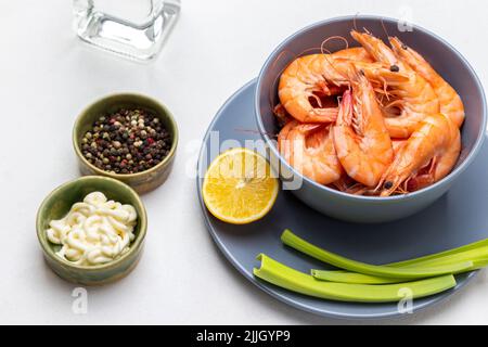 Gekochte Garnelen auf einer grauen Schüssel. Lauch und Zitrone auf dem Teller. Weiße Sauce und Piment in Schalen. Draufsicht. Weißer Hintergrund Stockfoto