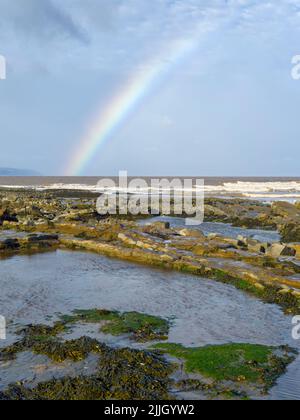 Ein Regenbogen über dem Bristol Channel vom East Quantoxhead Beach an der Küste von Somerset, England. Stockfoto