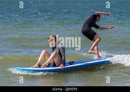 Stand-up-Paddleboarding, zwei ungeschickte Mädchen, die auf dem Paddleboard/SUP-Board auf See trainieren, um ihr Gleichgewicht zu halten Stockfoto