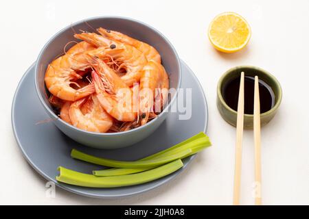 Essstäbchen und Sojasauce in der Schüssel. Garnelen in einer grauen Schüssel und Sellerie-Stängel auf dem Teller. Draufsicht. Weißer Hintergrund Stockfoto