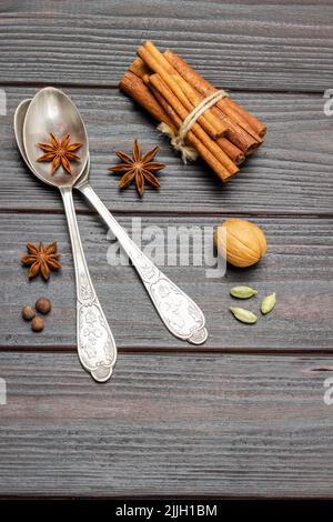 Zwei Metalllöffel und Sternanise. Die Zimtstangen werden zu Bündeln gebunden. Flach liegend. Dunkler Holzhintergrund. Stockfoto