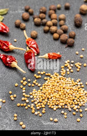 Senfkörner, trockene Paprikaschoten und Piment auf dem Tisch. Draufsicht. Schwarzer Hintergrund Stockfoto