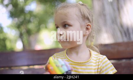 Kleines Mädchen hält bunte Lebkuchen. Nahaufnahme Porträt von niedlichen Mädchen auf Parkbank mit Cookies in schaut um. Stockfoto