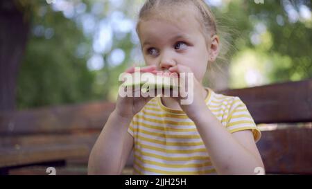 Nahaufnahme von niedlichen kleinen Mädchen isst Eis. Nahaufnahme eines Mädchens, das auf der Parkbank sitzt und Eis isst. Stockfoto