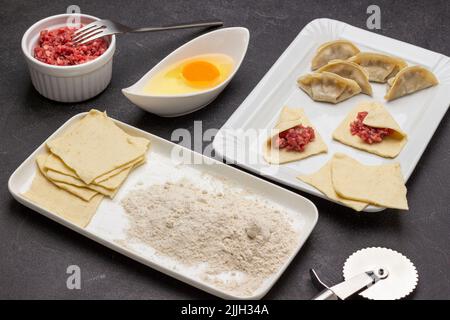 Mehl und Teigstücke auf dem Teller. Hackfleisch in einer Schüssel. Rohe khinkali-Knödel auf weißem Teller. Draufsicht. Schwarzer Hintergrund Stockfoto