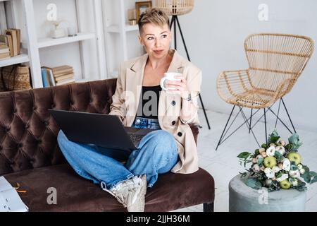 Schöne Hipster Frau in legeren Stoff mit Laptop zu Hause. Fröhliche Frau mit Laptop Stockfoto