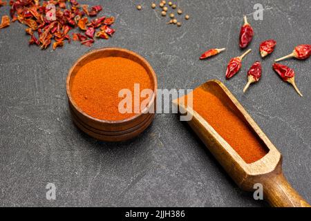 Paprika in einer Kugel und einer Holzschale gemahlen. Paprika auf dem Tisch. Nahaufnahme. Flach liegend. Schwarzer Hintergrund Stockfoto