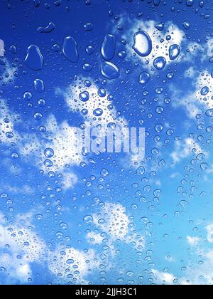 Eine vertikale Aufnahme von Wassertropfen des Regens auf dem Fenster unter einem bewölkten Himmel Stockfoto