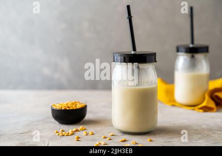 Vegane, gesunde Erbsenmilch in Gläsern mit Trinkhalmen, betontem Hintergrund, Erbsenkörnern und Mockup-Platz Stockfoto