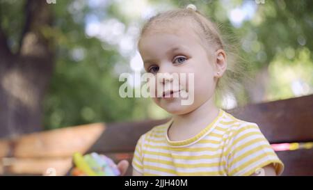 Odessa, Ukraine, Osteuropa. 26.. Juli 2022. Kleines Mädchen hält einen bunten Lebkuchen und lächelt. Nahaufnahme Porträt von niedlichen Mädchen auf Parkbank mit Cookies in Blick in die Kamera-Objektiv sitzen. (Bild: © Andrey Nekrasov/ZUMA Press Wire) Stockfoto