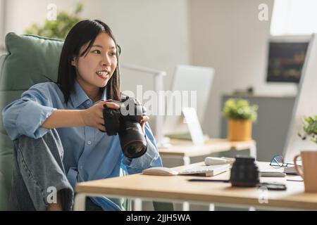 Fröhliche Vietnamesische Frau Fotograf Hält Fotokamera Sitzen Am Arbeitsplatz Stockfoto