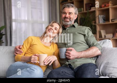 Ehepaar Mittleren Alters Verbringt Zeit Zu Hause, Trinkt Kaffee Und Schaut Fern Stockfoto