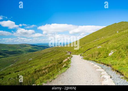 SNOWDON, WALES - 09. JULI 2022: Wanderer gehen vom Mount Snowdon aus nach dem Erreichen des Gipfels in der Morgendämmerung. Stockfoto