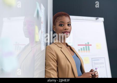 Porträt einer selbstbewussten afroamerikanischen jungen Geschäftsfrau, die sich im Konferenzraum auf das Whiteboard stützt Stockfoto