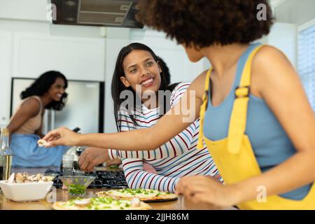 Lächelnde biracial junge Frau, die Freund beim Zubereiten der Pizza auf Kücheninsel zu Hause ansieht Stockfoto