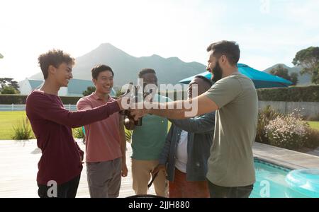 Multirassische männliche Freunde toasten Bierflaschen, während sie sich auf der Grillparty im Hinterhof amüsieren Stockfoto