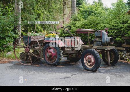 Alte Oldtimer-Traktor oder landwirtschaftliche Fahrzeug für die Anzeige. Gebrochener rostiger Tracktor mit Blumen verziert. Stockfoto