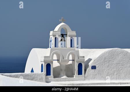 Oia, Santorini, Griechenland - 2022. Juni: Glocken auf der Spitze einer Kirche mit Blick auf das Meer in der Stadt Oia. Stockfoto