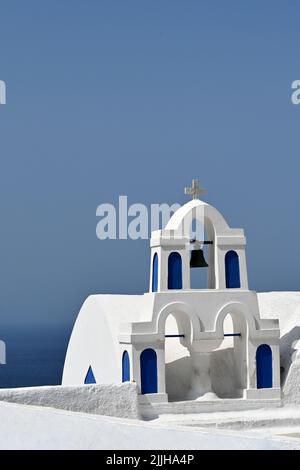 Oia, Santorini, Griechenland - 2022. Juni: Glocken auf der Spitze einer Kirche mit Blick auf das Meer in der Stadt Oia. Stockfoto