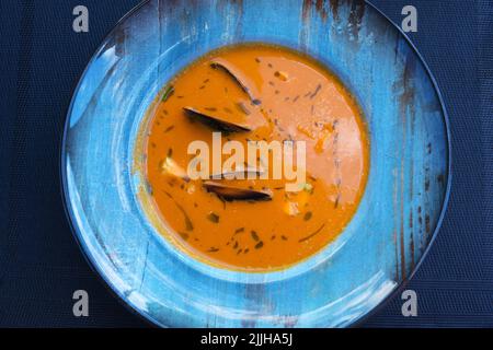 Köstliche Meeresfrüchte Tomatensoße mit Bouillabaisse Fischsuppe mit Garnelen, Muscheln und Fisch auf einem blauen Teller auf dem Tisch. Köstliches romantisches Abendessen in einer Fischruhe Stockfoto