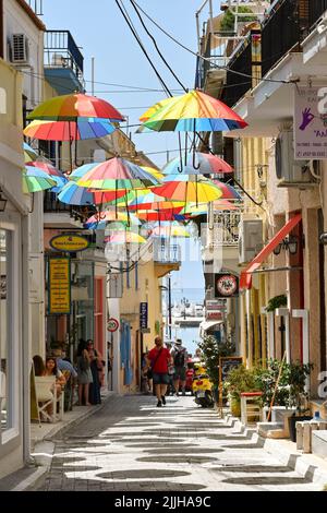 Aegina, Griechenland - Mai 2022: Farbige Sonnenschirme hängen über einer der engen Straßen der Stadt Aegina Stockfoto