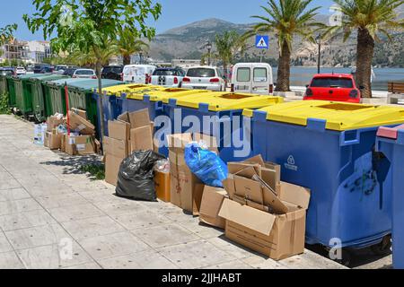 Argostili, Kefalonia, Griechenland - Juni 2022: Ich habe Kartons auf einer Straße in der Stadt gegen große Industrieabfallbehälter gestapelt Stockfoto