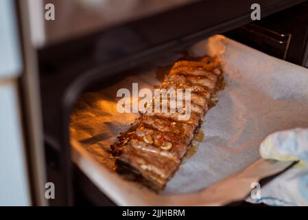 Das Mädchen nimmt die gebackenen Schweinerippen aus dem Ofen Stockfoto