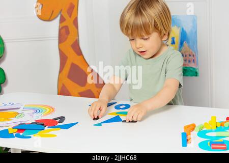 Blonde Jungen bilden Formen stehen am Tisch im Kindergarten Stockfoto